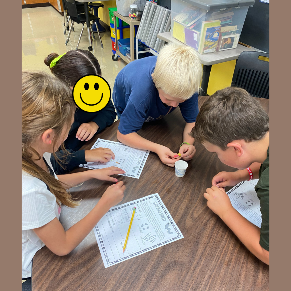 Elementary students observing and taking notes about a gummy worm on a paper cup