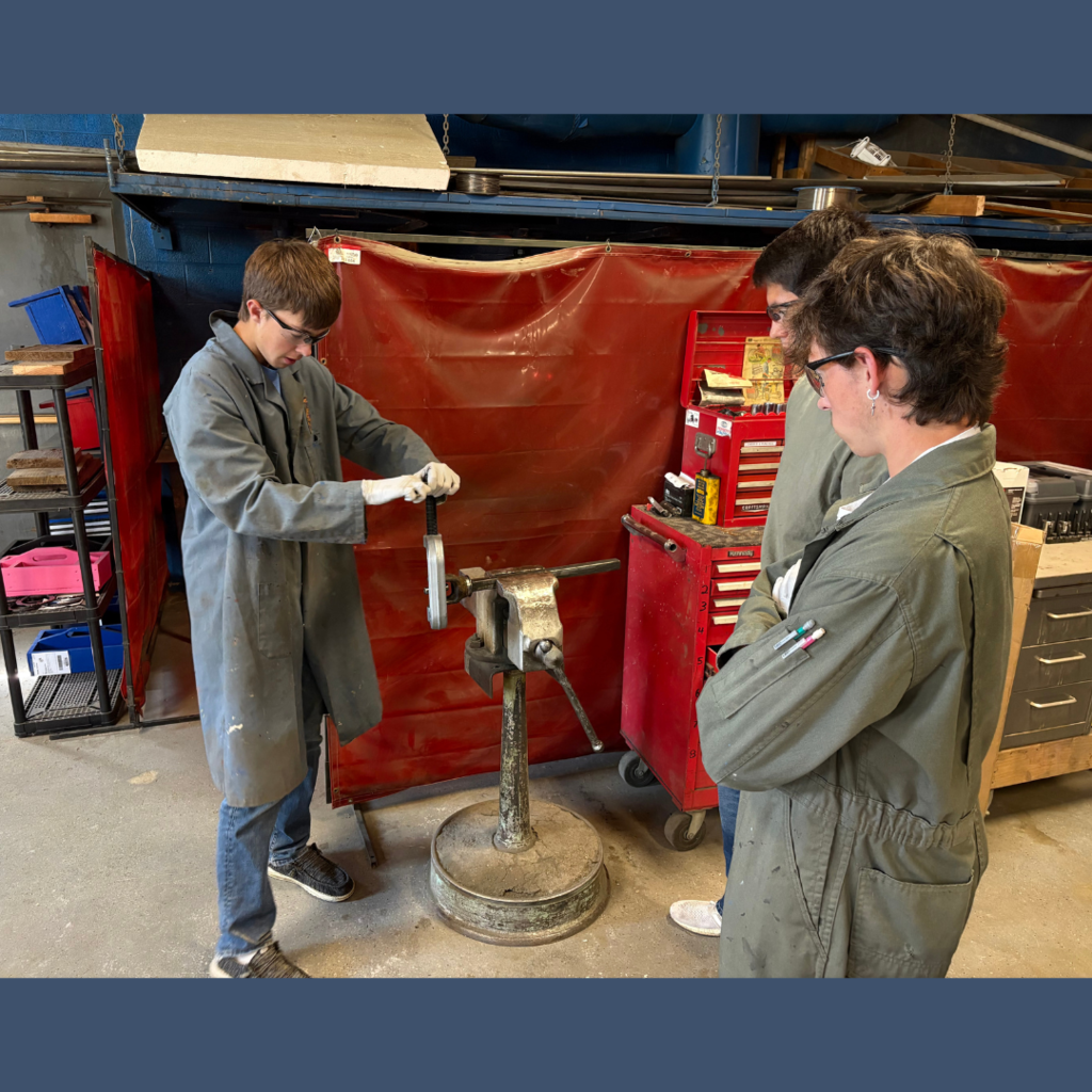 A high school student testing machinery parts in an ag lab while two others look on