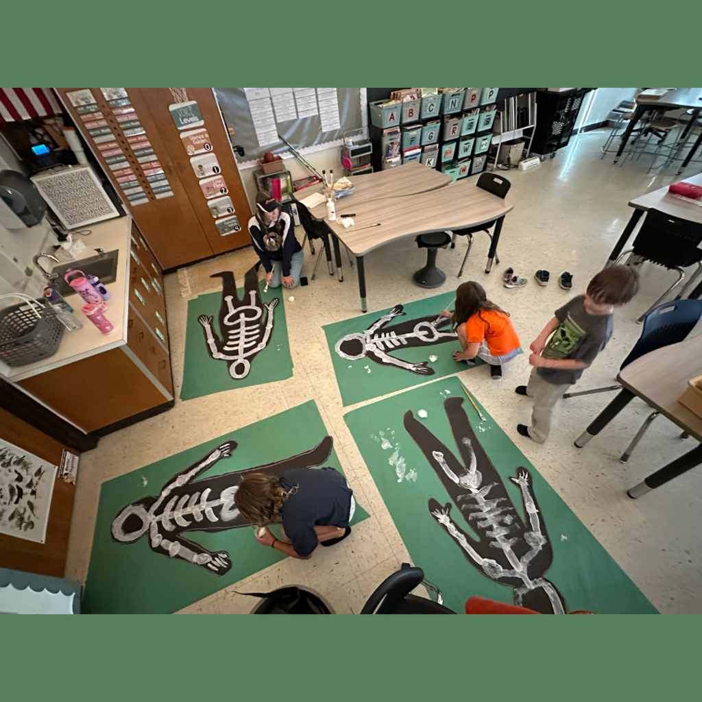 Elementary students posing with life-sized shadow cutouts with painted on skeleton bones