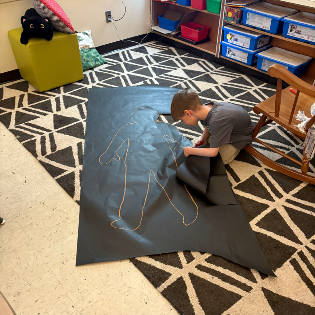 Elementary student cutting out a life-sized shadow cutout.