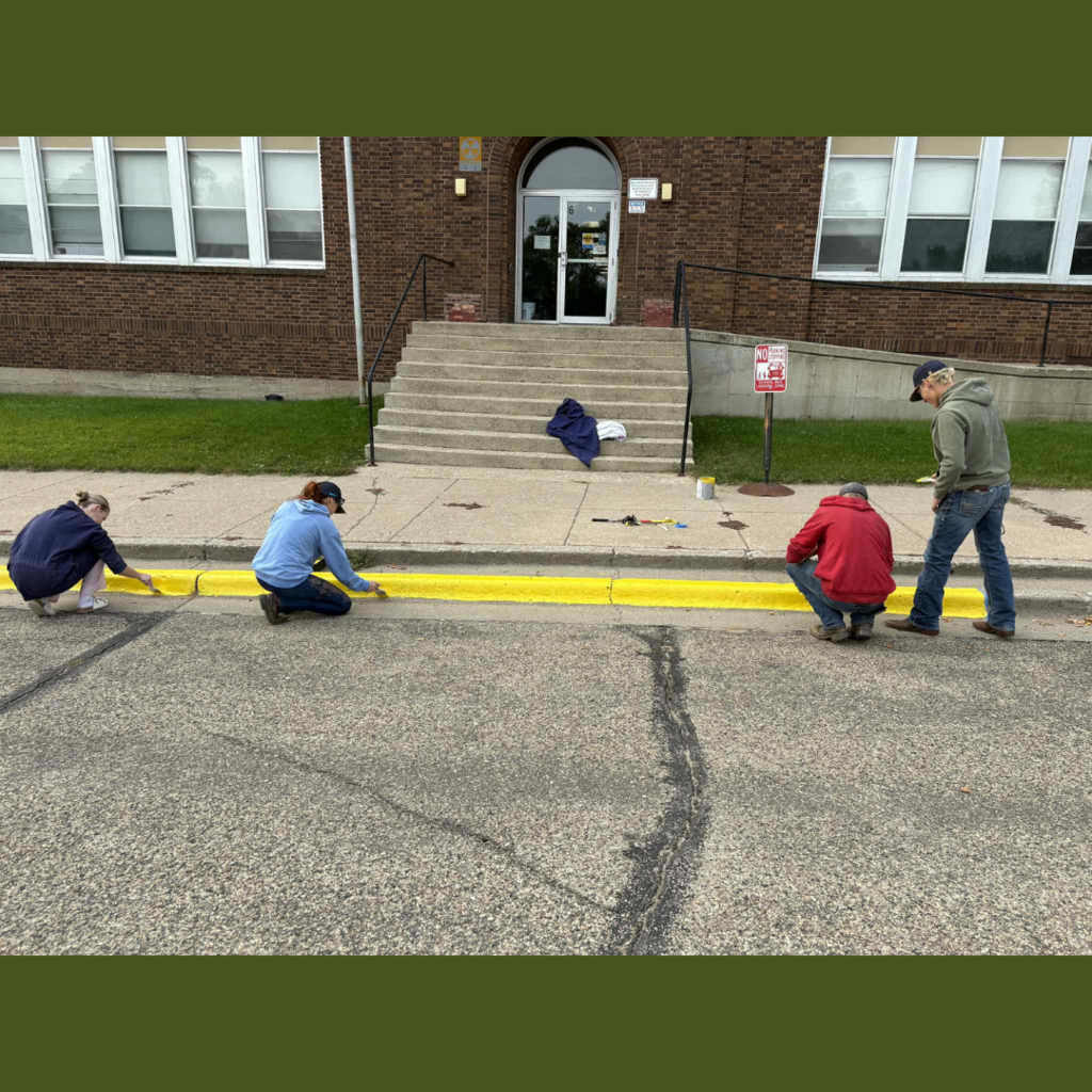 High school students painting the yellow curb in front of a school