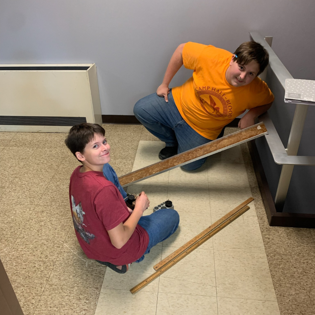 Two high school students rolling cars down a ramp