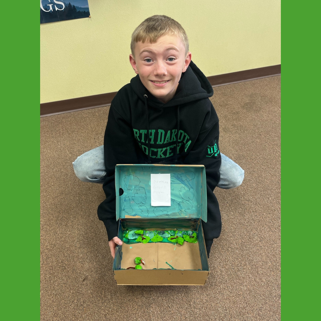 A sixth grade student showing off his homemade shoebox biome