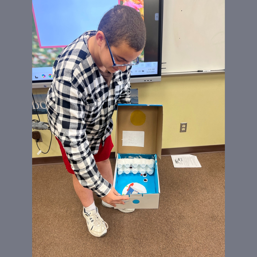 A sixth grade student showing off his homemade shoebox biome