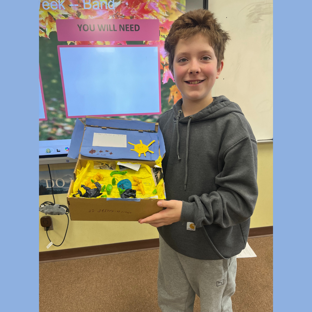 A sixth grade student showing off his homemade shoebox biome