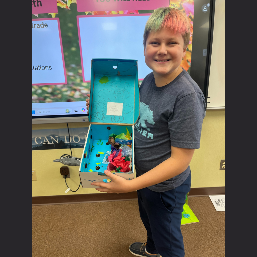 A sixth grade student showing off his homemade shoebox biome