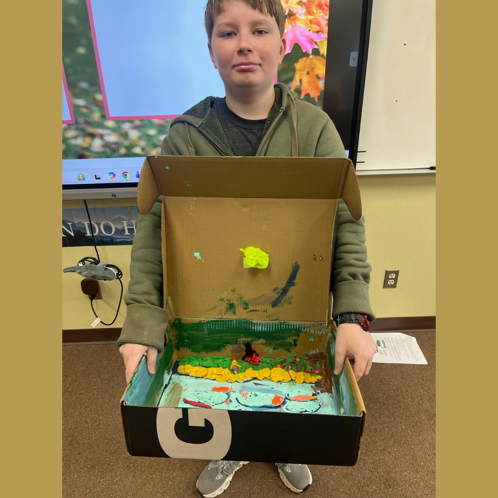 A sixth grade student showing off his homemade shoebox biome