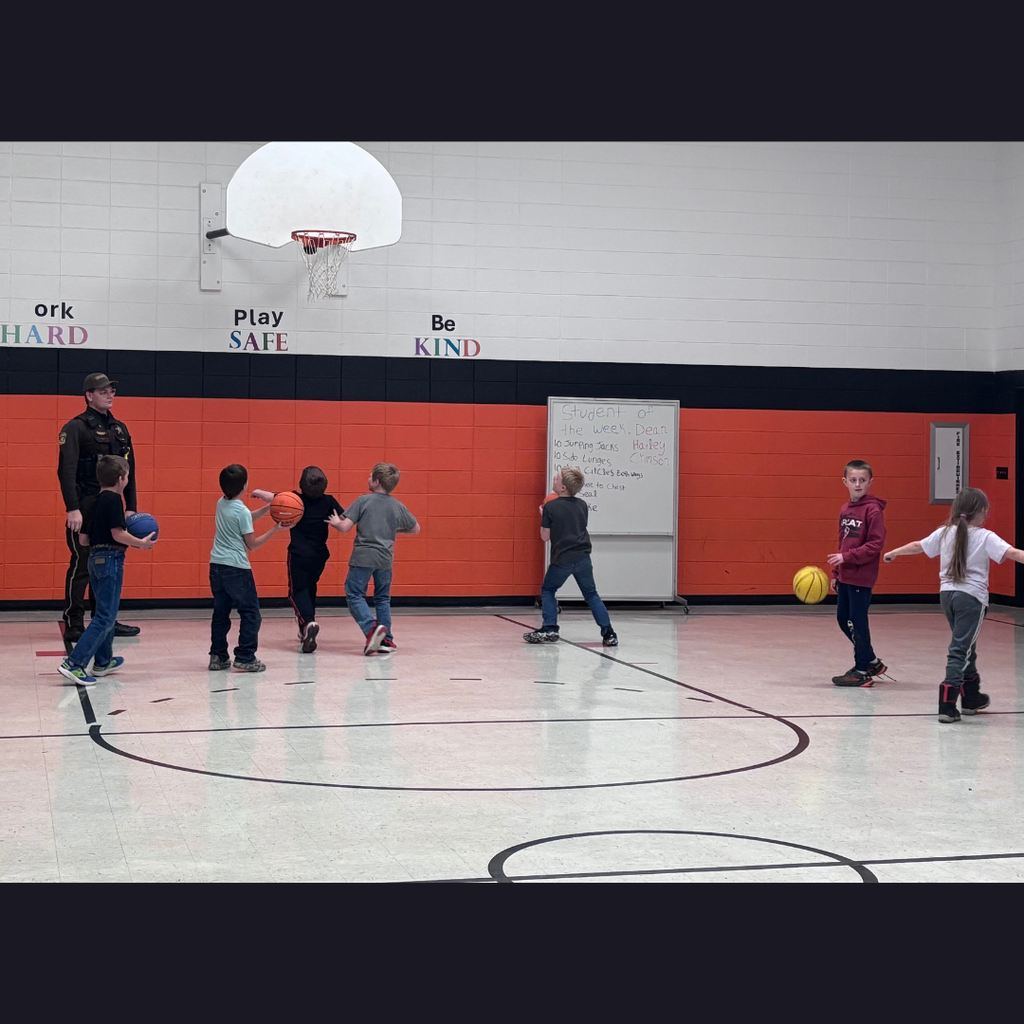 A school resource officer playing basketball with elementary students