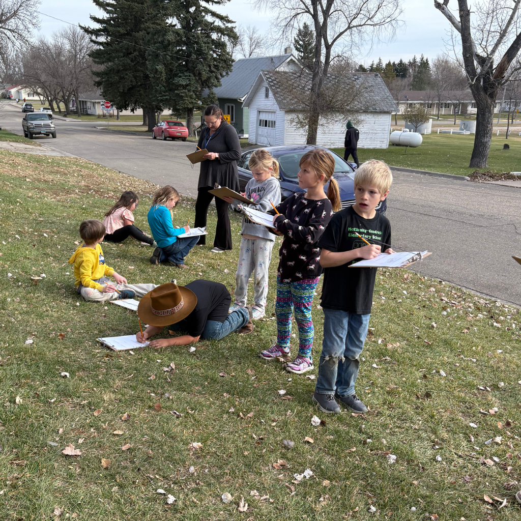 Lower elementary students holding clipboards and drawing outside