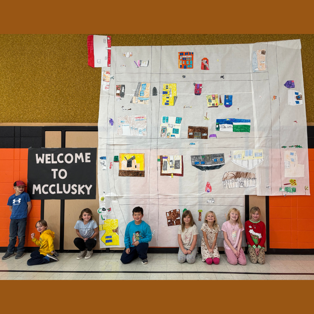 Lower elementary students posing in front of their large poster of the town
