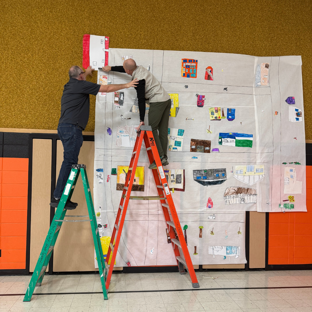 Two men standing on ladders taping a large poster to a school wall