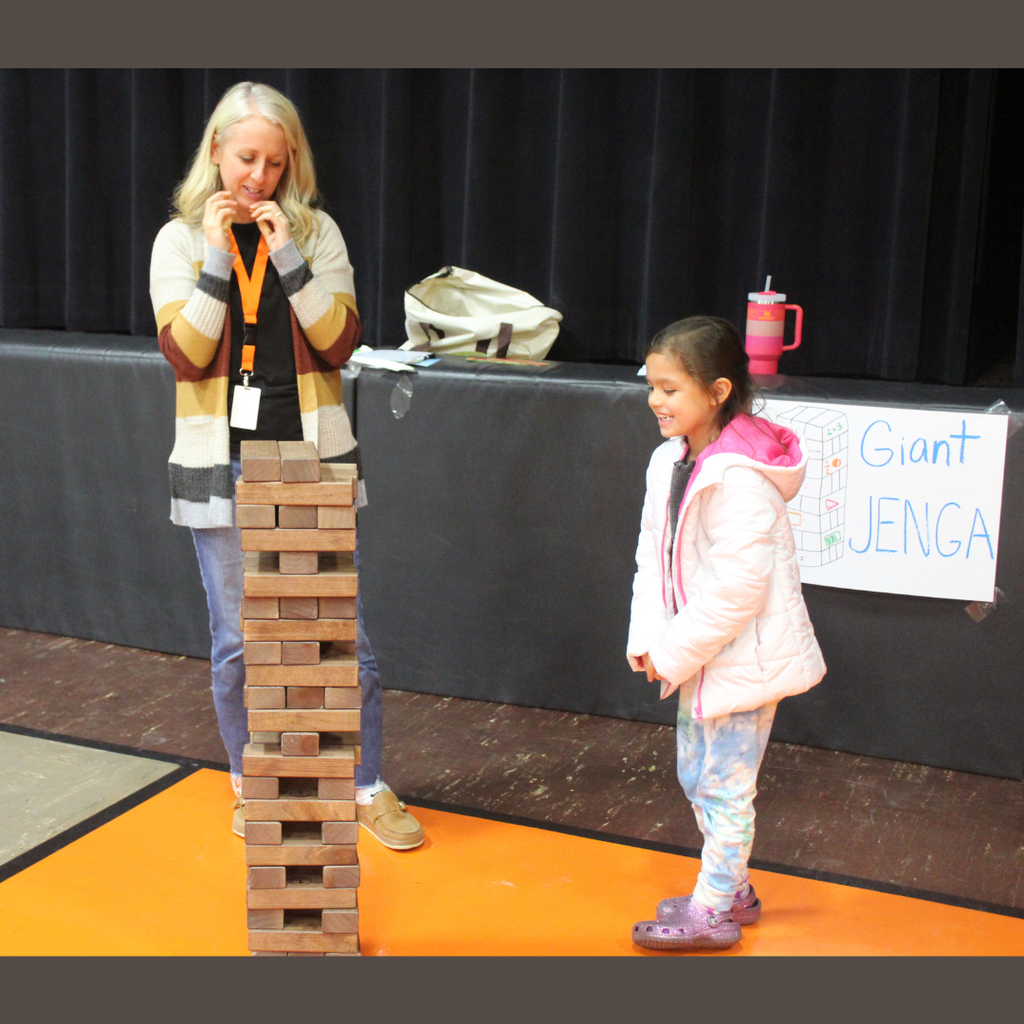 A small elementary student playing giant Jenga with a teacher
