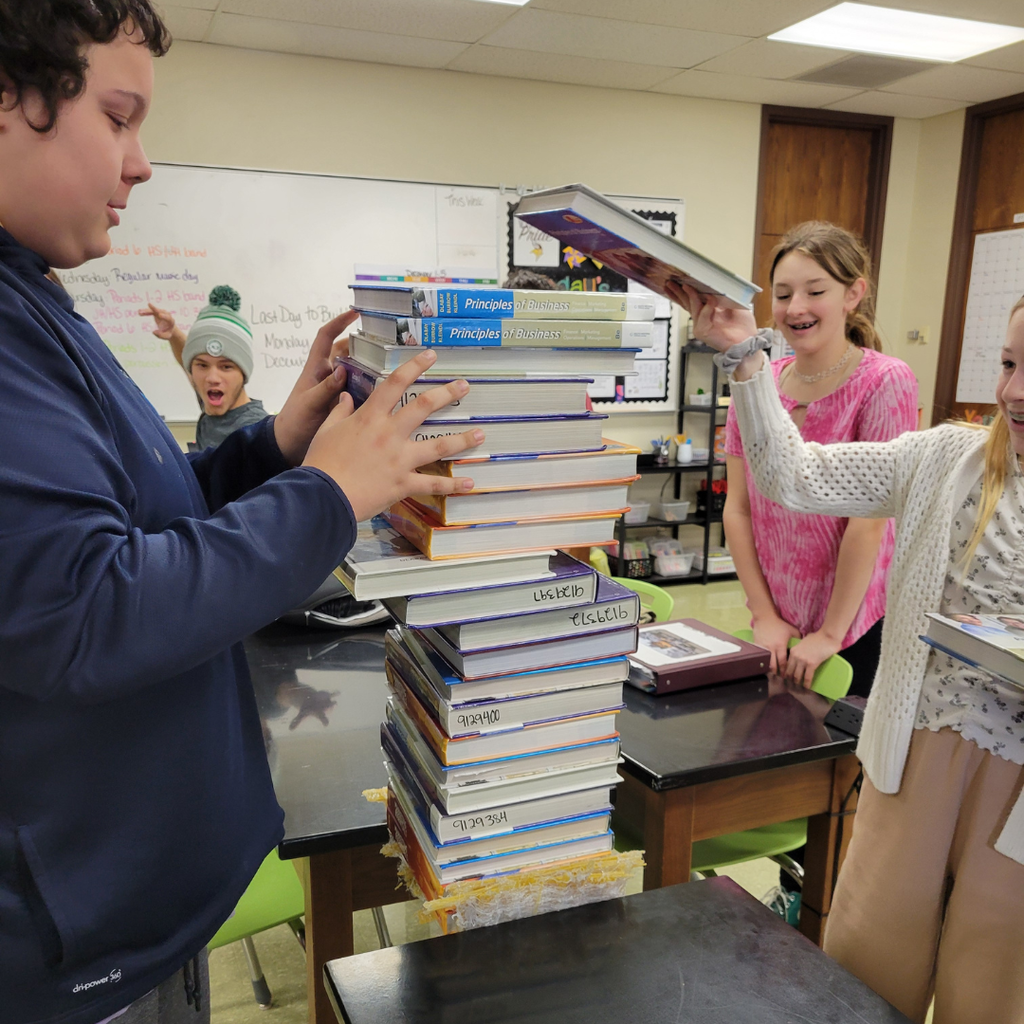 Junior high students stacking textbooks on top of their spaghetti bridge