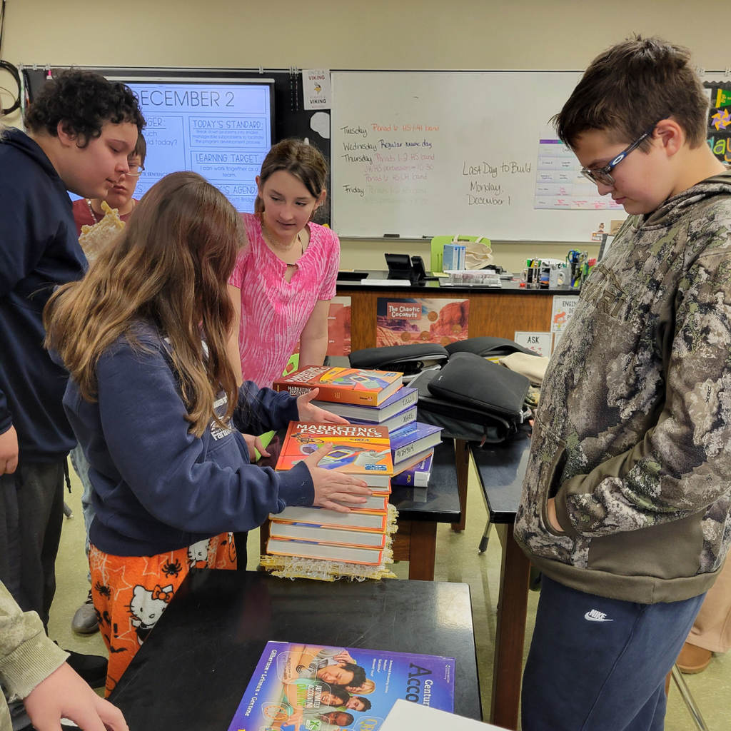 Junior high students stacking textbooks on top of their spaghetti bridge