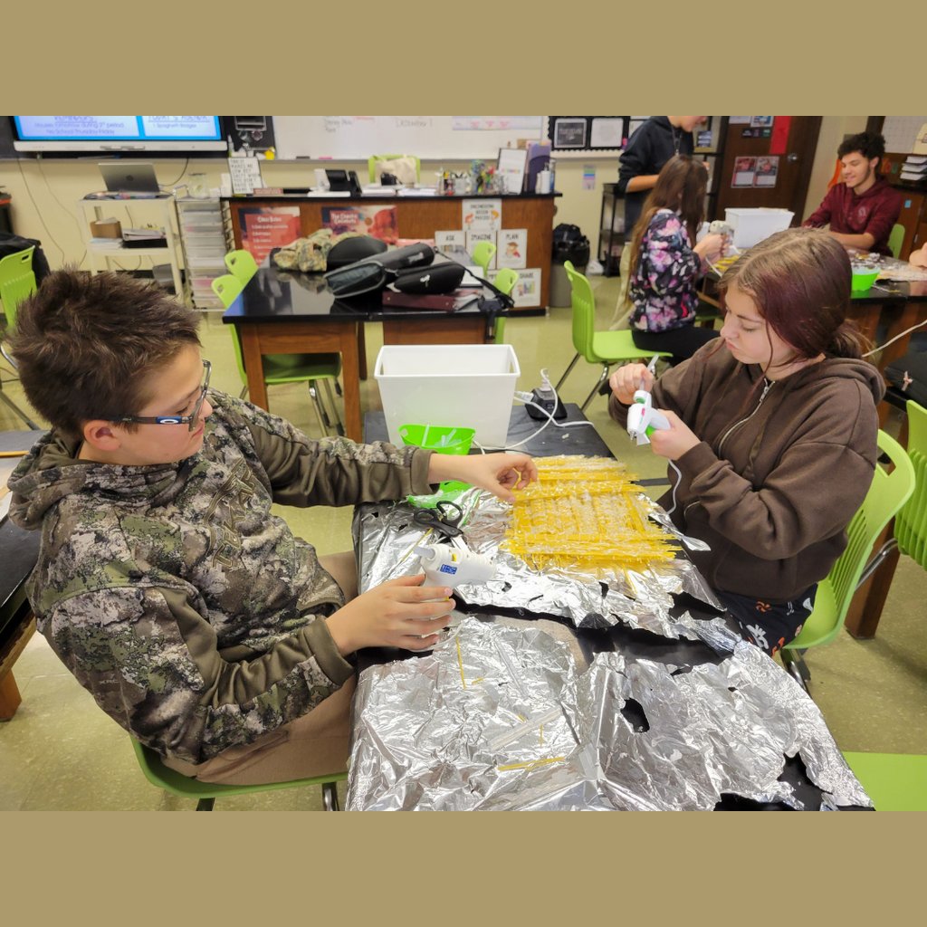 Junior high students building a bridge out of dry spaghetti noodles and hot glue