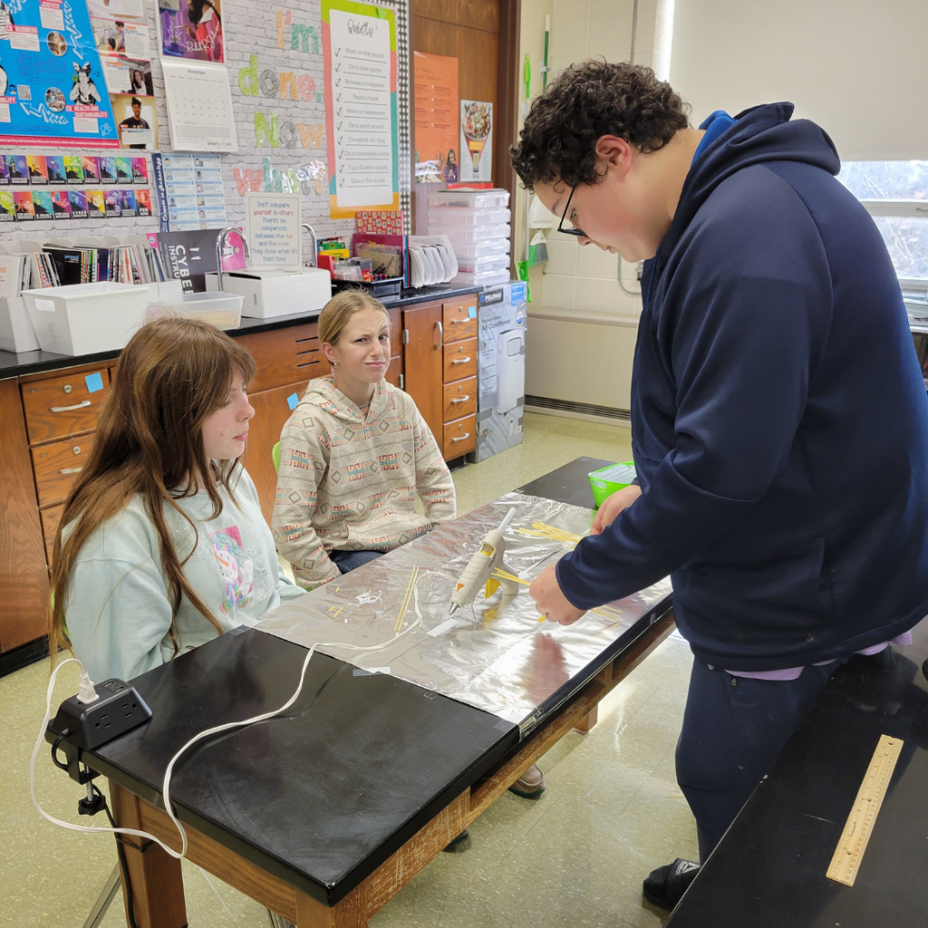 Junior high students building a bridge out of dry spaghetti noodles and hot glue