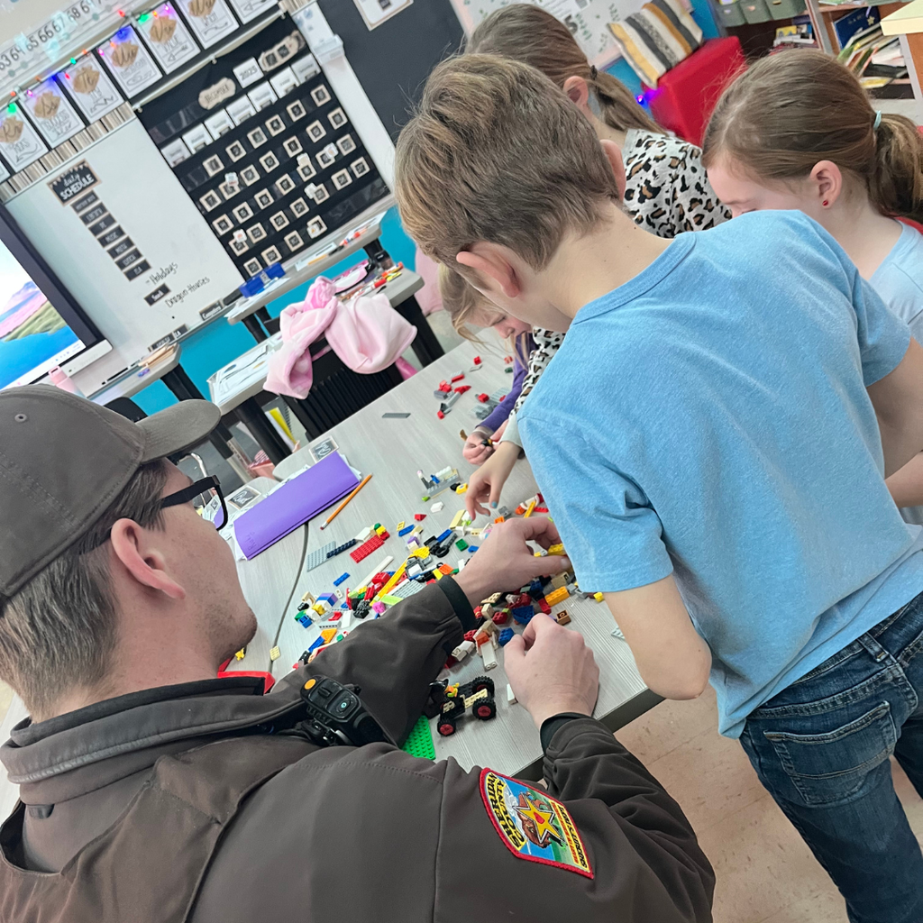 Elementary students sitting around a table playing with Lego with a deputy sheriff