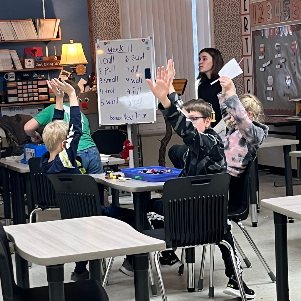 Elementary students sitting at desks and raising their hands