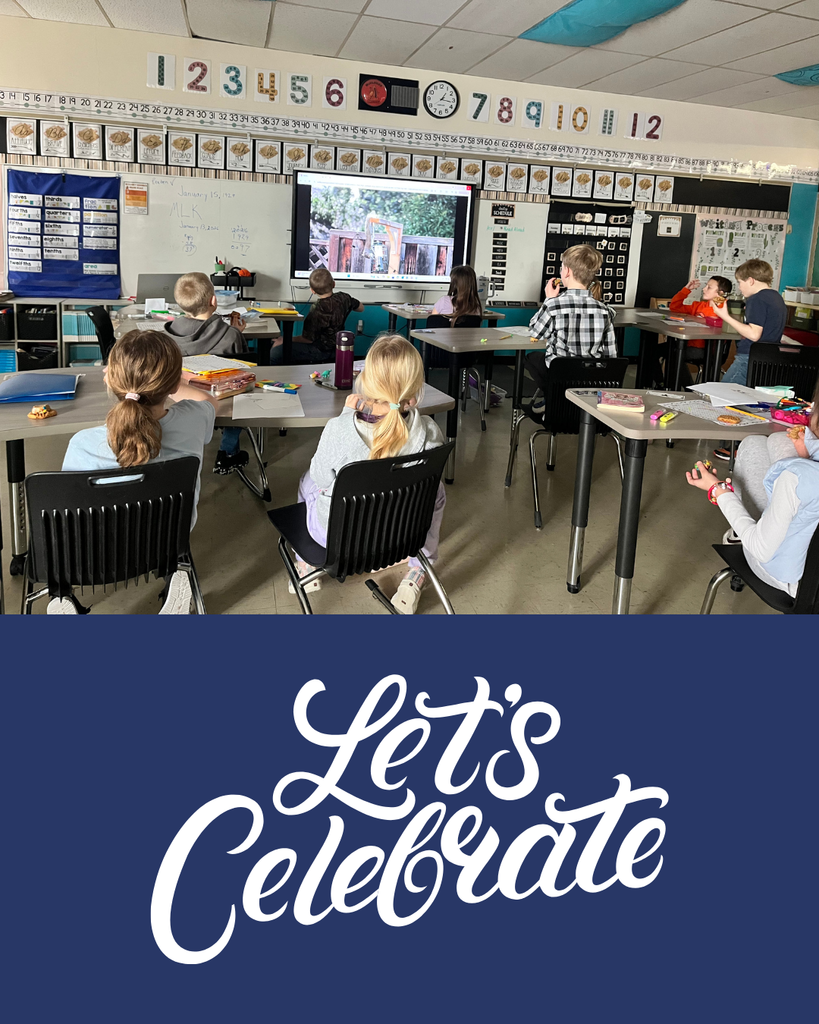 Young elementary students sitting in their desks, eating snacks and watching a video