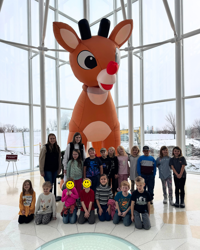 Lower elementary students posing with their teachers and a giant blow-up Rudolph