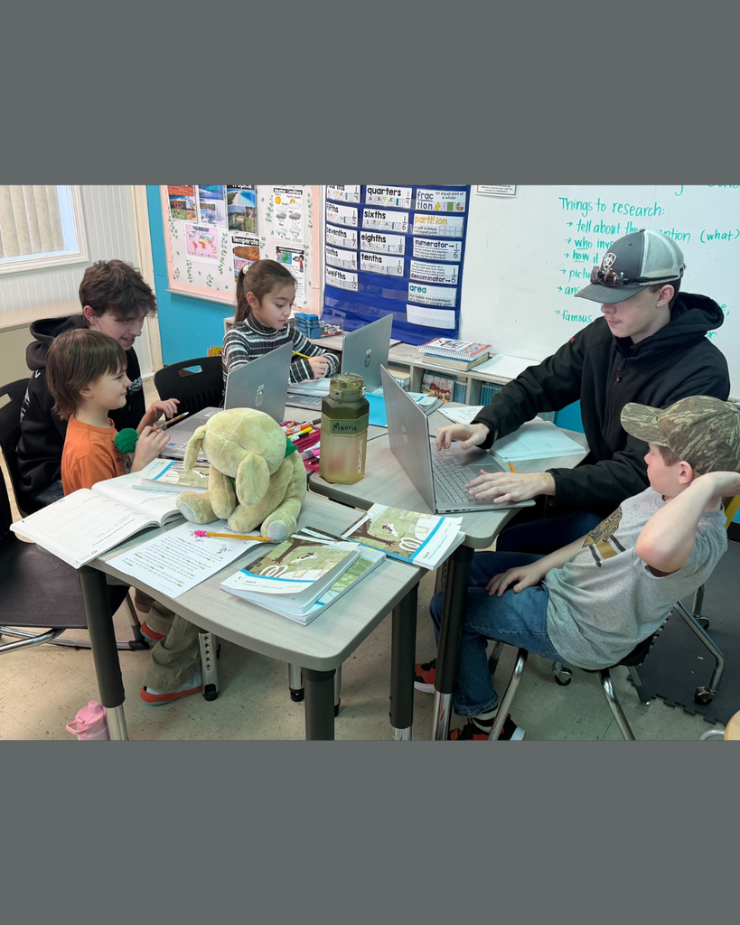 Elementary students and their high school mentors conducting research on their computers.