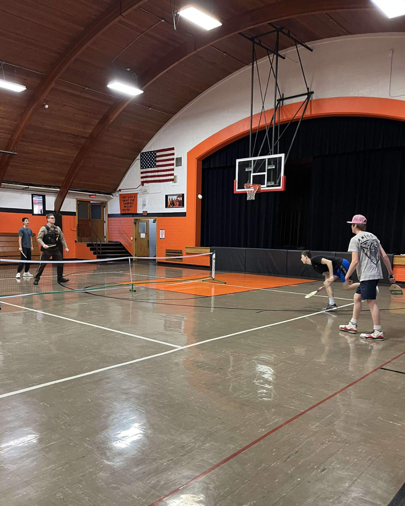 A deputy sheriff playing pickleball in a high school gym with three teenage boys.