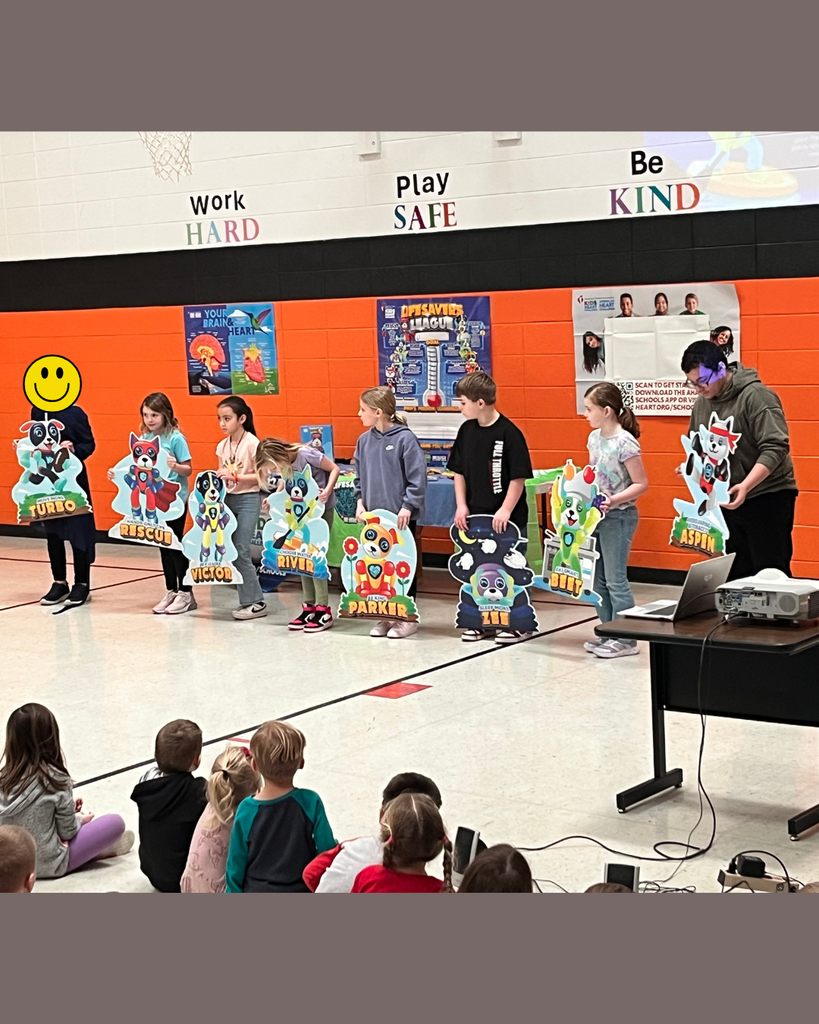 Elementary students holding up signs showing the American Heart Association characters.