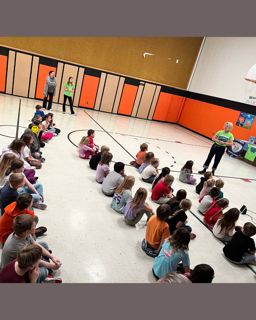Elementary students sitting on a gym floor listening to an American Heart Association representative.