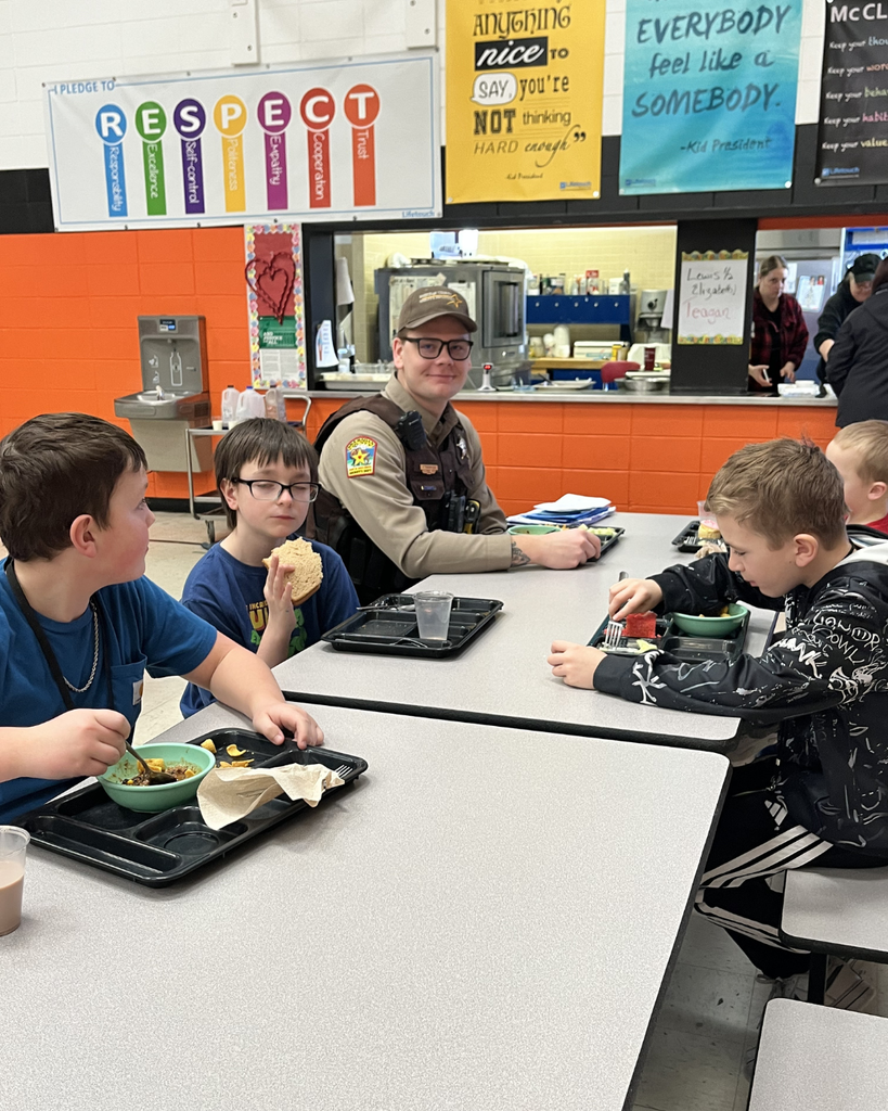 A male school resource officer sitting at the lunch table with upper elementary boys.