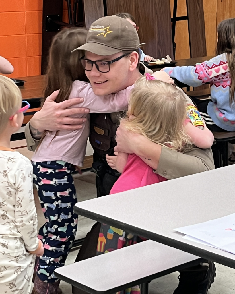 A male school resource officer getting hugs from lower elementary girls