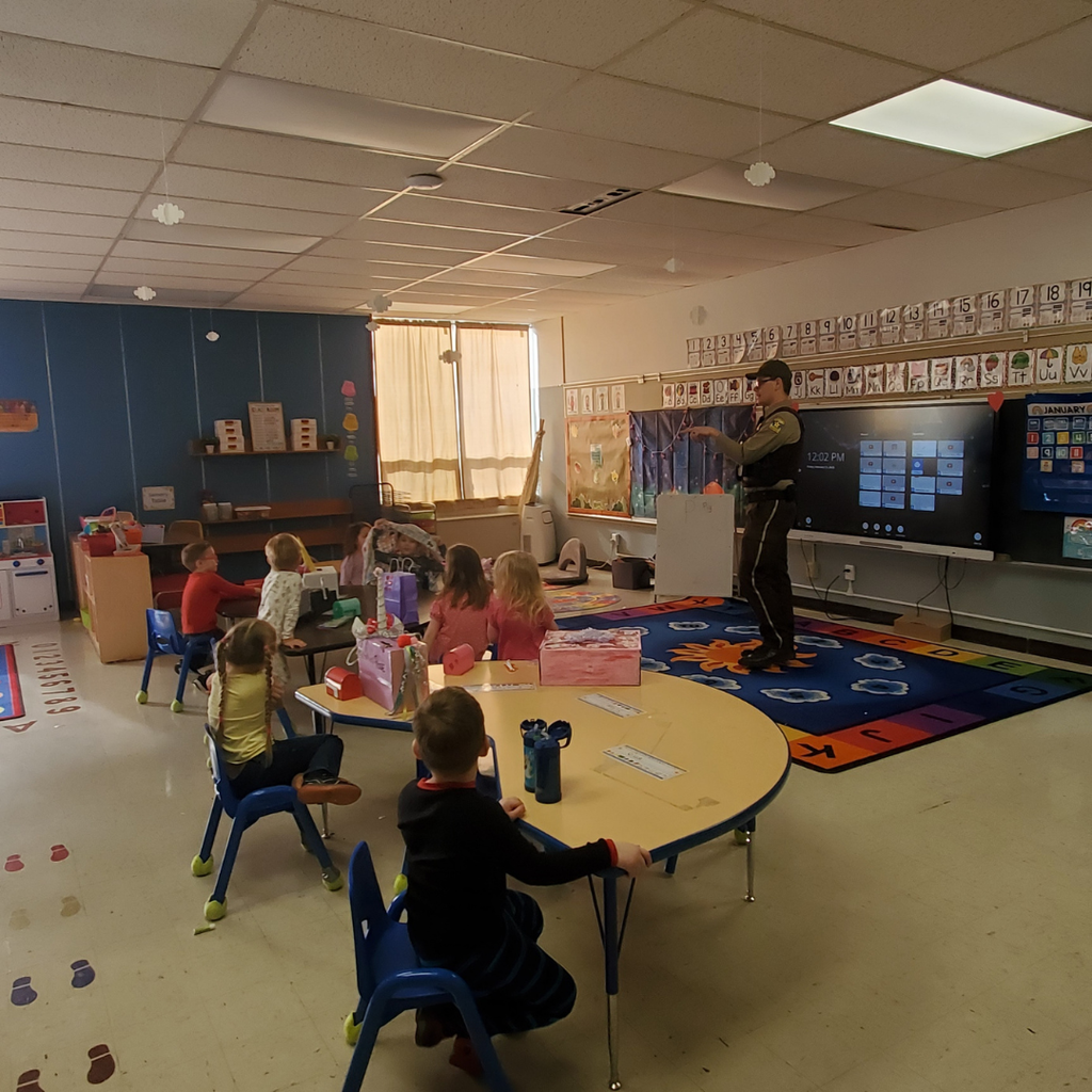 Preschool students sitting at their desks listening to the School Resource Officer speak