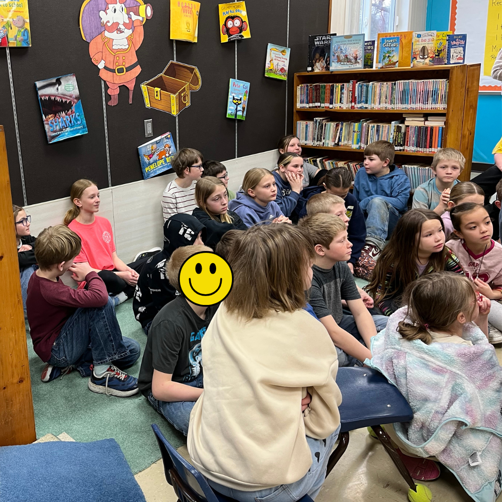 Elementary students sitting in a library listening to a speaker