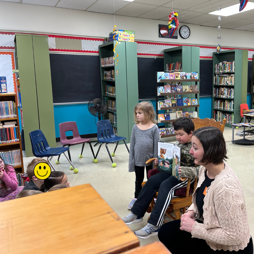 Elementary students gathered around an adult author reading her book