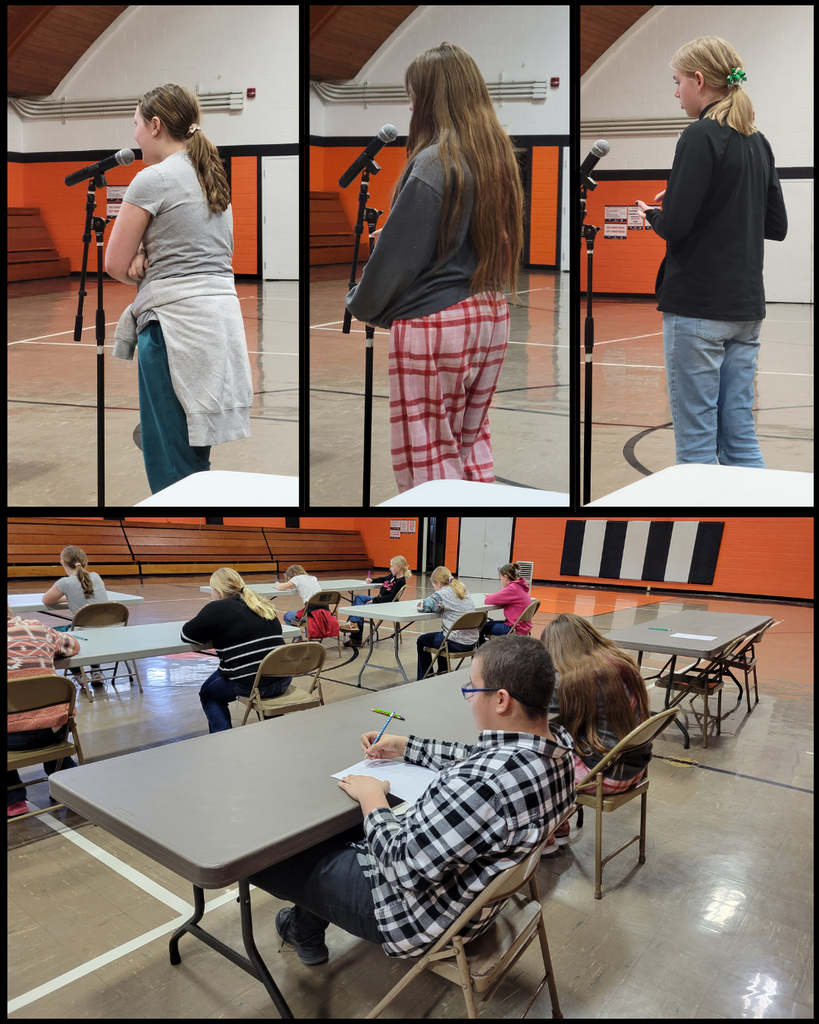 Three junior high students standing at a microphone, with more junior high students sitting at tables and writing on paper
