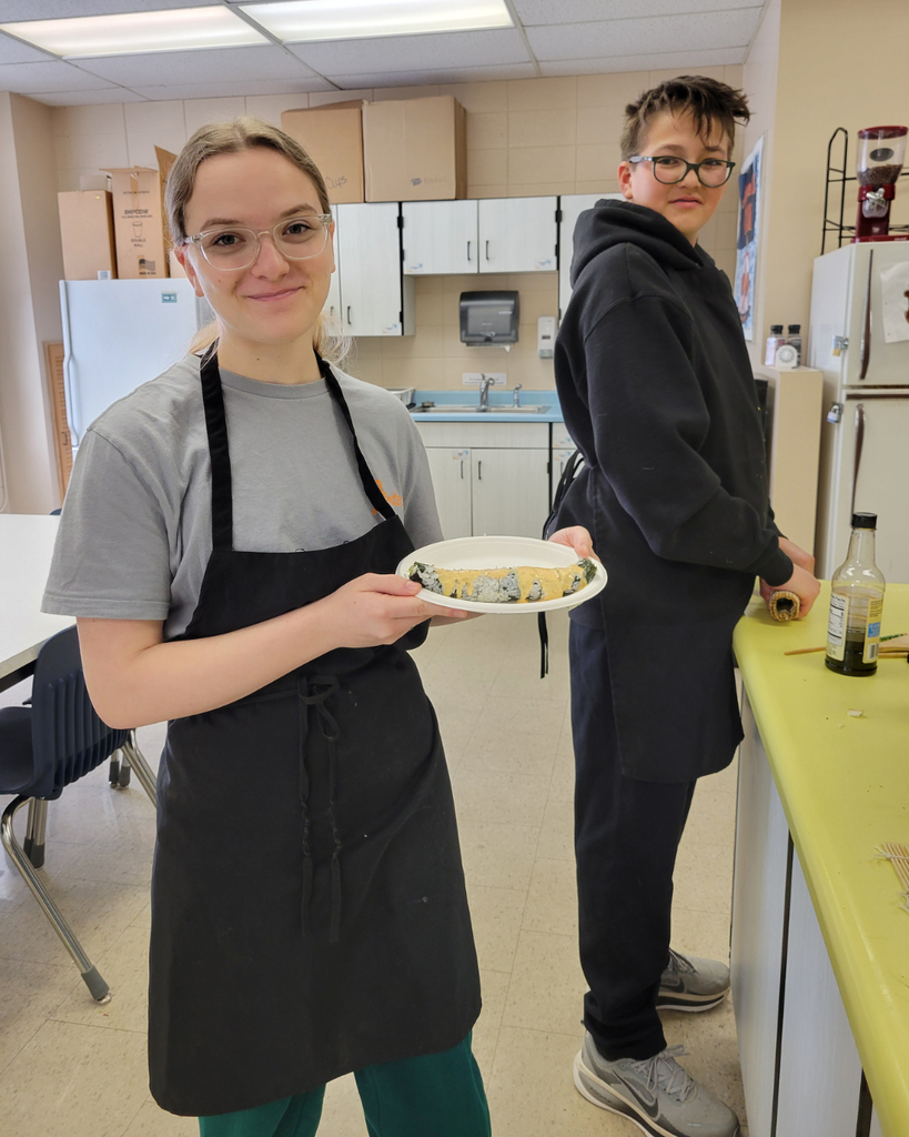 A high school student holding up her sushi roll while another looks on