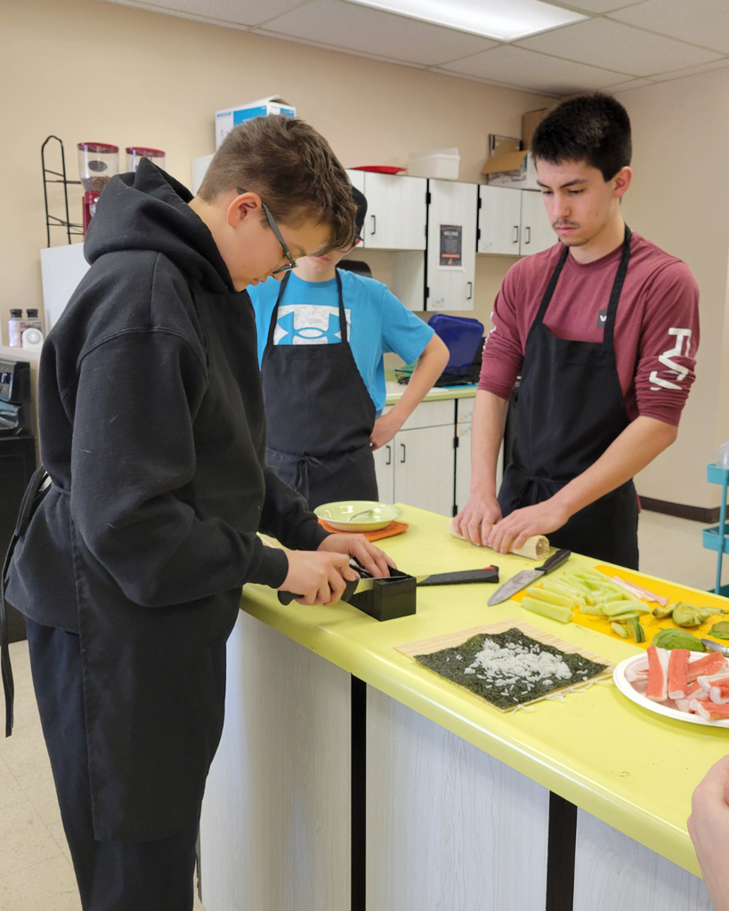 Two high school students making sushi in a kitchen setting