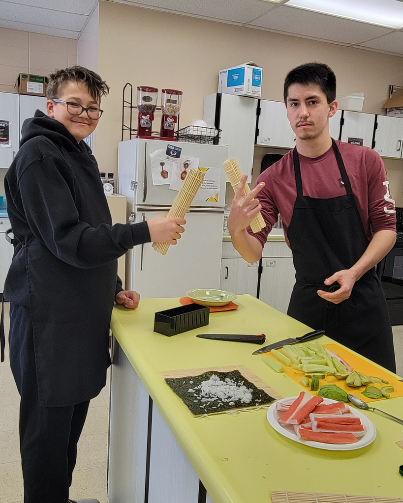 Two high school students holding up their rolled sushi