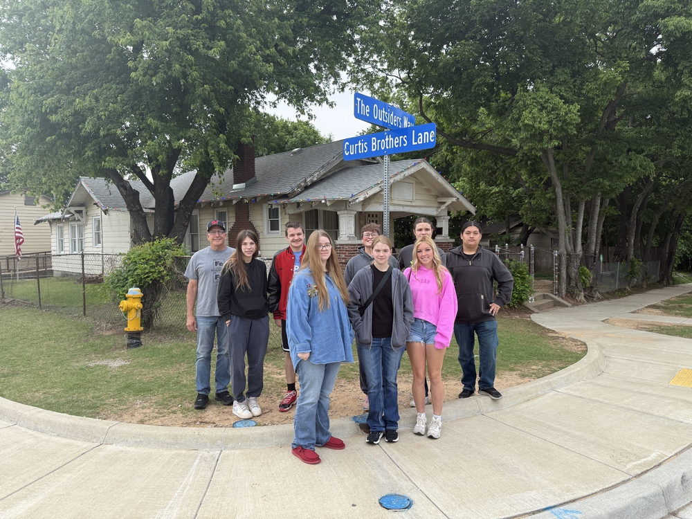 Students standing at intersection in front of Outsiders House museum. 
