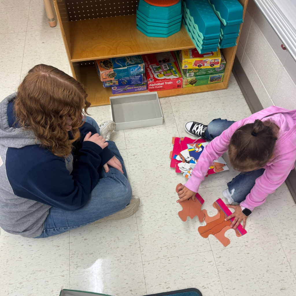 GIrl watching a little girl put together a puzzle. 