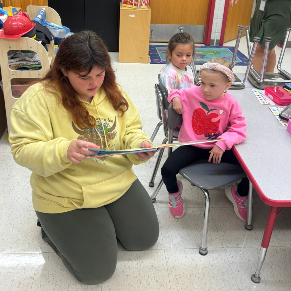 Girl reading to two girls listening