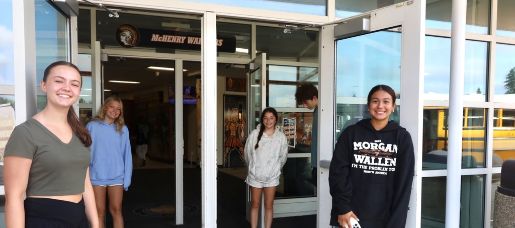 Four students smiling and holding the door 