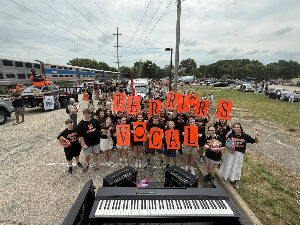 Vocal Warriors holding sings that spell at Vocal Warriors with keyboard in front of them at Fiesta Days parade 