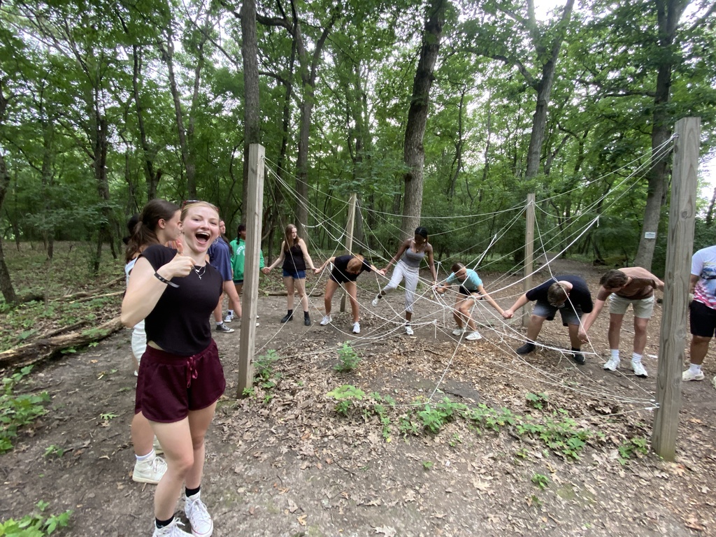 Student giving a thumbs up with students holding hands near  ropes course