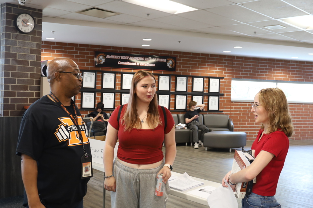 Students talking to staff, one holding books