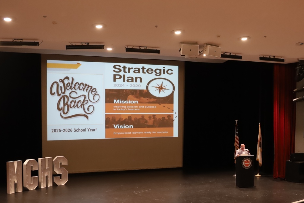 Dr. McTague speaking with Strategic Plan slide that says Welcome Back 2025-2026 school year and an MCHS decorative piece on stage