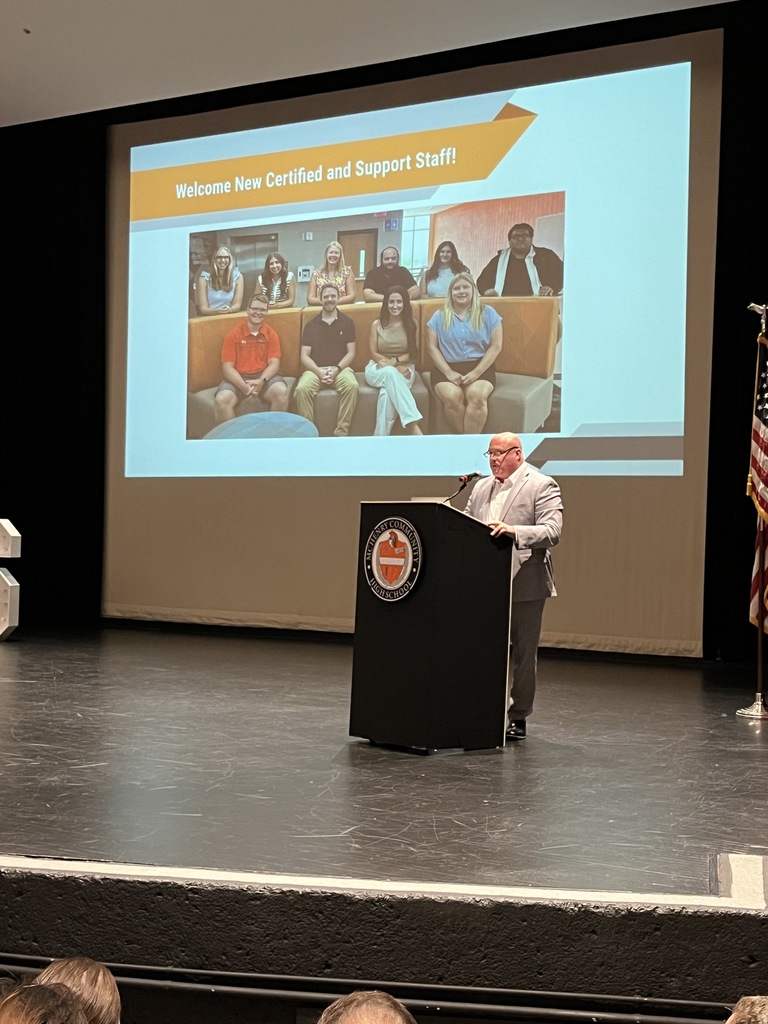 Dr. McTague on stage in front of New Certified and Support staff photo