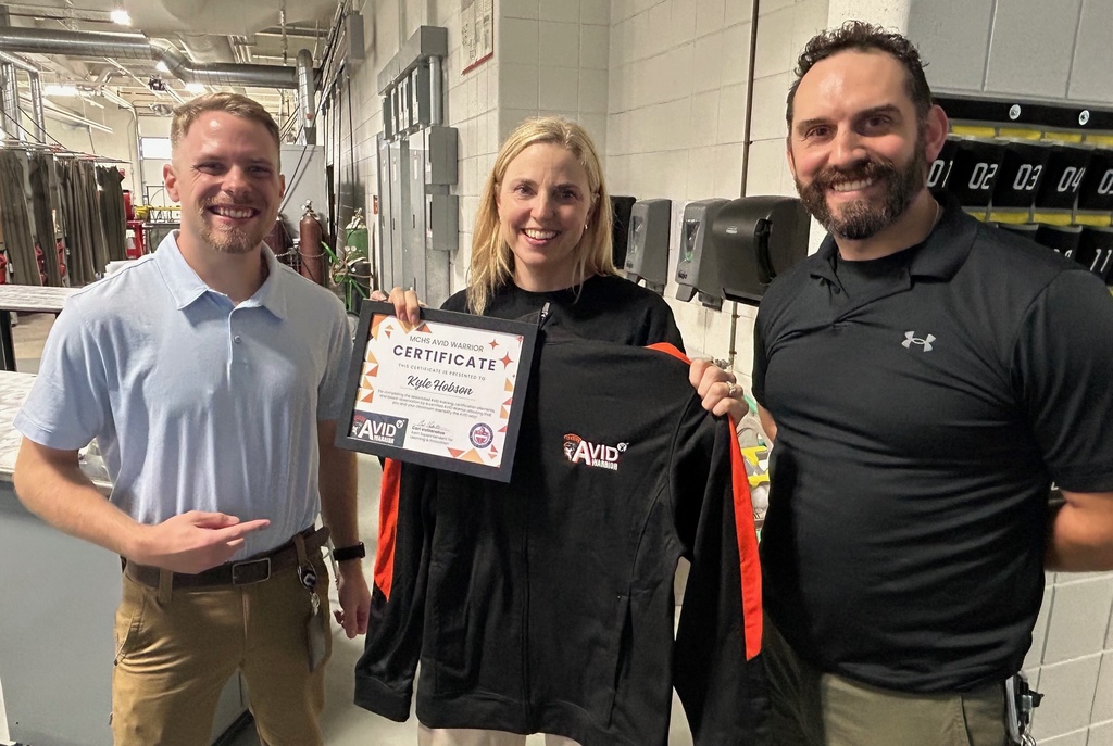 Kyle holding her certificate and Avid shirt next to two teachers