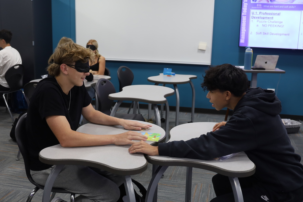 Two students working on a puzzle, one blindfolded 