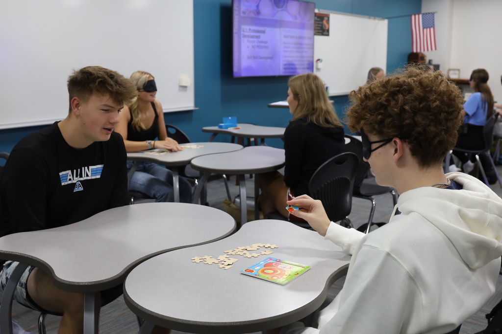Two students working on a puzzle, one blindfolded 