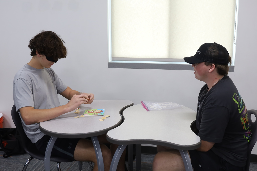 Two students working on a puzzle, one blindfolded 
